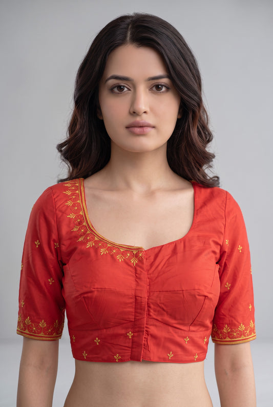 A woman wearing a red short-sleeve blouse with gold embroidery on the neckline and sleeve cuffs, photographed against a plain light gray studio background.