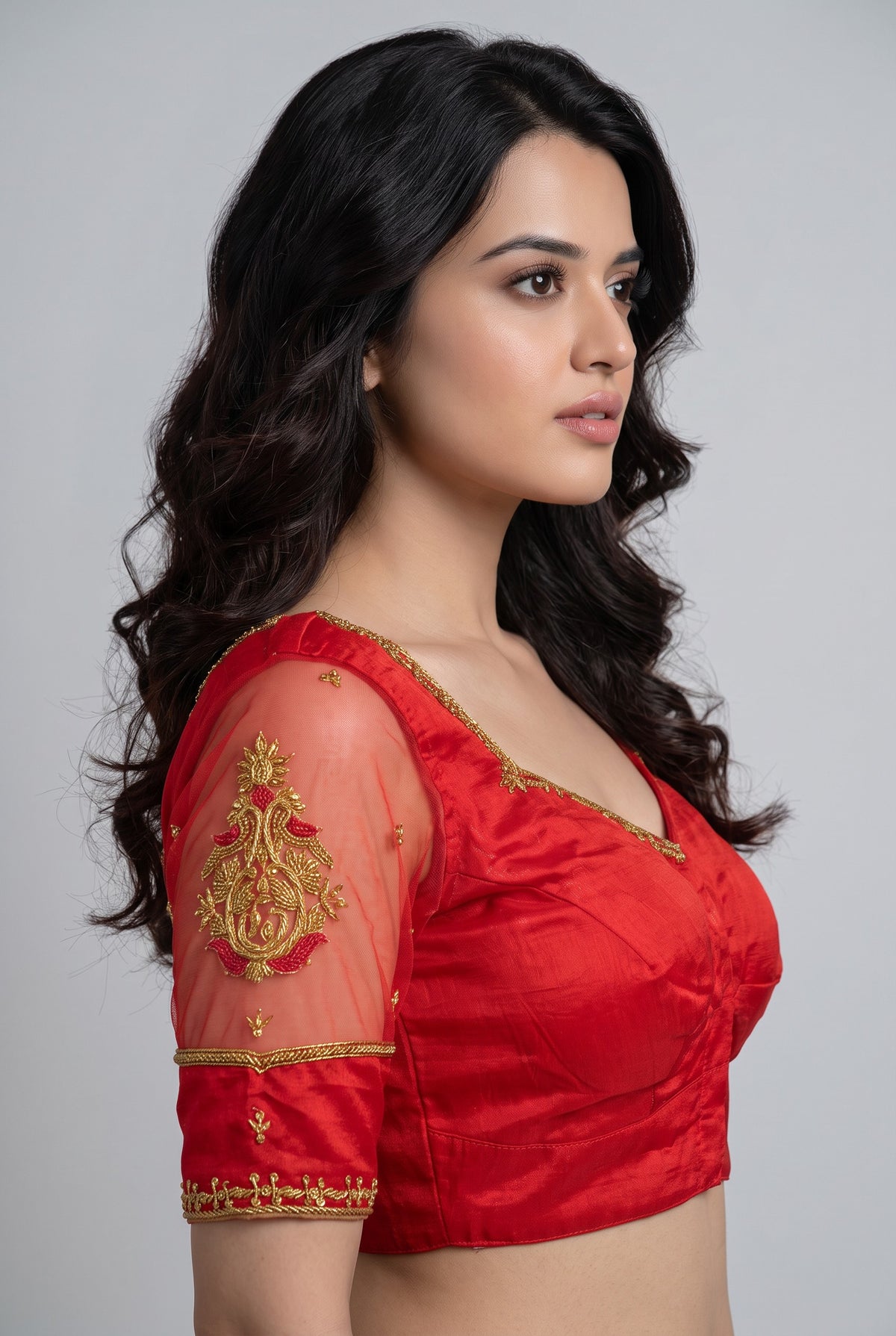 A woman shown in side profile wearing a bright red traditional blouse with gold embroidery and sheer sleeves, photographed against a plain light gray studio background.